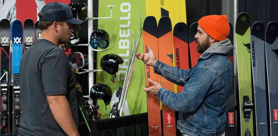 A guy asking a gear rep about skis at a booth at Snowvana