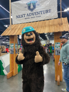 Next Adventure sign with a bear mascot in front doing thumbs up at Snowvana